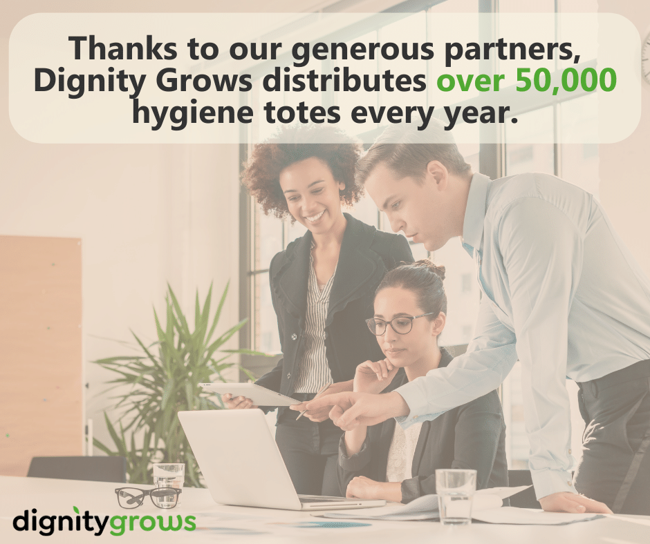 Corporate workers stand around a desk. Text reads "Thanks to our generous partners, Dignity Grows distributes over 50,000 hygiene totes every year.